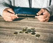 primo piano delle mani di una persona anziana che svuota sul tavolo le monetine di un portafoglio vuoto (Foto Belchonock@123RF.com)