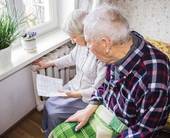 Una coppia di anziani seduti davanti al termosifone con una bolletta in mano