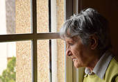 Anziana donna triste guarda dai vetri di una finestra chiusa