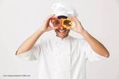 Un cuoco regge simpaticamente sul viso due peperoni aperti al centro come fosse un paio di occhiali (Foto Vadymvdrobot@123RF.com)