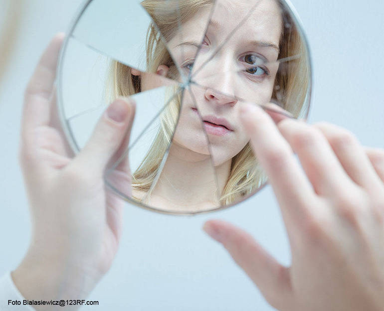 Giovane ragazza tiene tra le mani uno specchi rotto che riflette la sua immagine "spezzettata" (Foto Bialasiewicz@123RF.com)