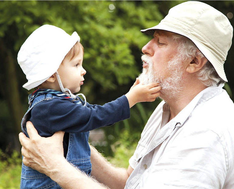 Un anziano signore tiene in braccio un bambino che gioca con la sua barba