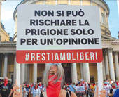 Manifestante in primo piano che regge un cartello con su scritto: "Non si può rischiare la prigione solo per u n'opinione. #restiamoliberi"