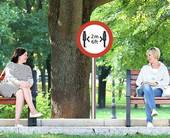 Due donne dialogano sedute su due panchine ai giardini separate da un segnale di distanziamento