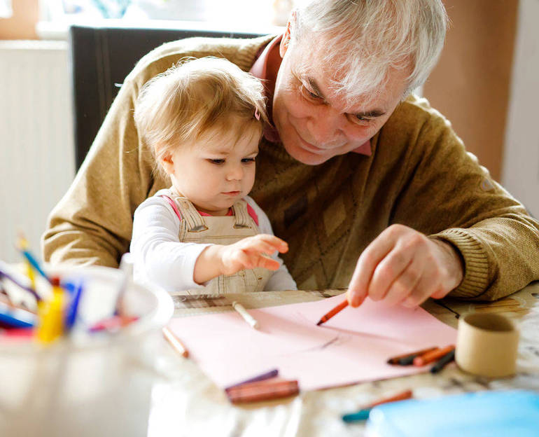 Un nonno aiuta la nipotina a fare un disegno