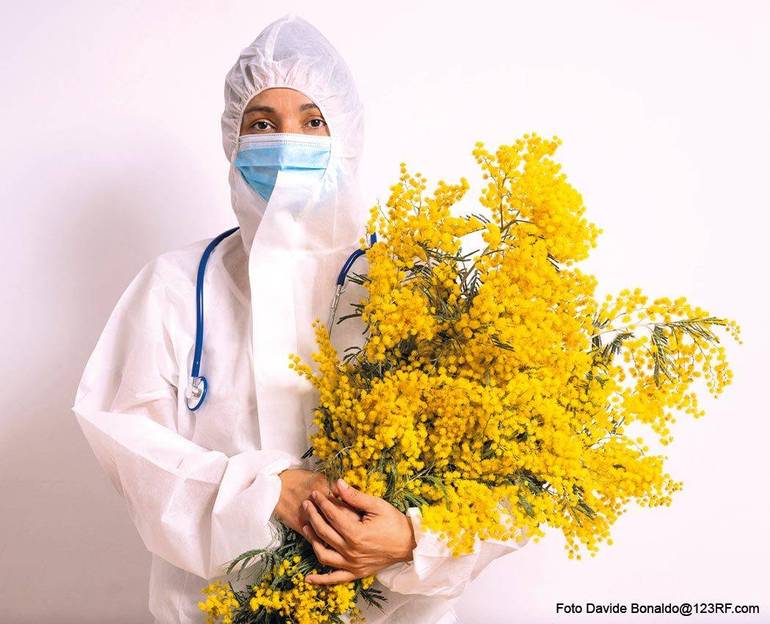 Operatrice sanitaria completamente bardata per proteggersi dal contagio Covid-10 con in braccio un mazzo di mimose
