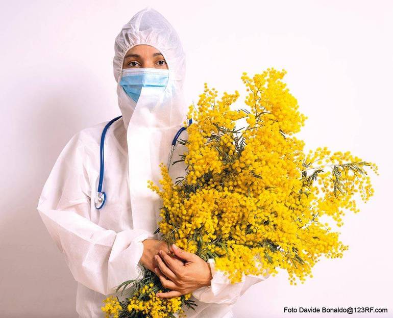 Operatrice sanitaria completamente bardata per proteggersi dal contagio Covid-10 con in braccio un mazzo di mimose Operatrice sanitaria completamente bardata per proteggersi dal contagio Covid-10 con in braccio un mazzo di mimose