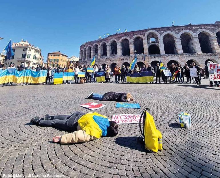 Manifestazione in piazza Bra con persone con bandiera ucraina stese per terra per ricordare le vittime della guerra