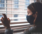 Giovane donna con mascherina guarda fuori dalla finestra attraverso le veneziane