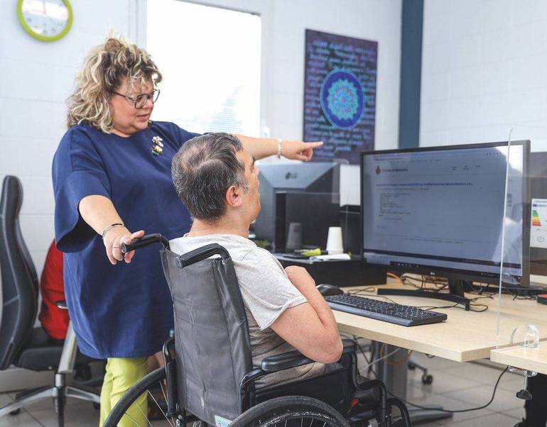 Persona con disabilità davanti al computer assistita da un'operatrice