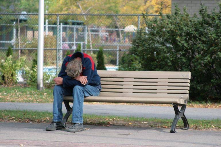 Uomo povero ripiegato su se stesso su una panchina