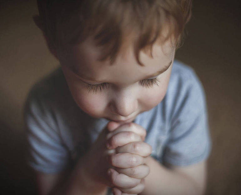 Bambino che prega con le manine giunte